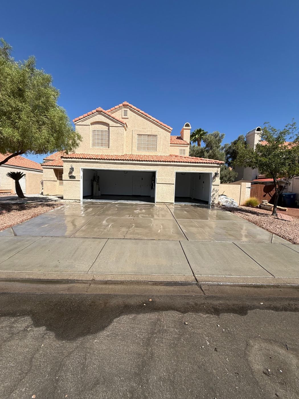 Freshly washed, still-wet concrete driveway in front of a tile-roof home with the three-car garage open